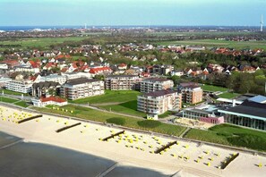 A coastal town with residential buildings, a beach with sun loungers, and a modern building with a glass facade. - Beach Palace, Apt. 220 (Cuxhaven)
