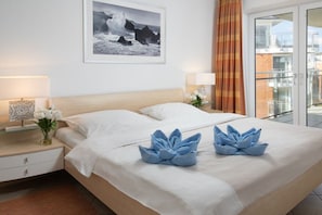 A hotel room with a bed, two bedside lamps, a framed photograph on the wall, and a view of the outside balcony. - Beach Palace, Apt. 220 (Cuxhaven)