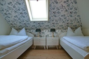 A bedroom with two single beds, a window, and a floral wallpaper pattern. - Beach grass - directly in Wyk (Wyk\/Föhr)