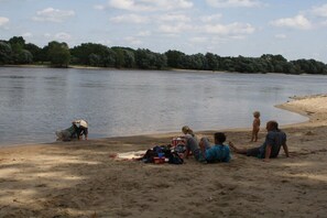 A lakeside scene with people sitting and standing on the sand, some near the water's edge. - Holiday home in Hitzacker with Wi-Fi (Hitzacker)