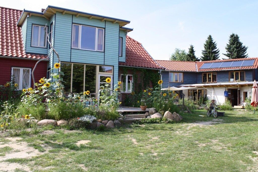 Una casa de dos pisos con techo de tejas rojas, fachada azul y un jardín con girasoles.