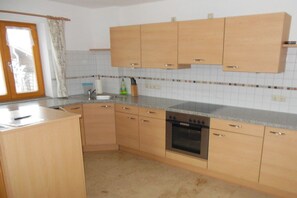 A kitchen with wooden cabinets, a built-in oven, and a window with a curtain. - Holiday farmhouse with 2 bedrooms (Nußdorf)