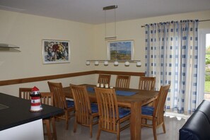Ein Essbereich mit Holztisch und Stühlen, einer schwarzen Arbeitsplatte, einer Leuchtturmdekoration und einem Fenster mit Karottenvorhängen.