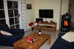 Uma sala de estar com sofá, mesa de centro com velas e copos de vinho, televisão e lareira.