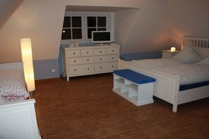 Ein Schlafzimmer mit Bett, Kommode, Schreibtisch, Fenster und Lampe.