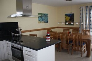 A kitchen with a central island, wooden dining table, and chairs. There is a stove, oven, and a range hood above the stove. - Holiday home in Usedom with 3 bedrooms (Heringsdorf)