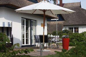 A building with a thatched roof, a white exterior, and a patio area with a table and chairs. - Holiday home in Usedom with 3 bedrooms (Heringsdorf)