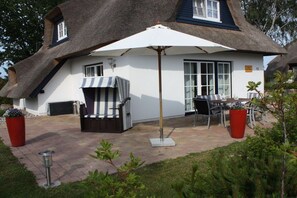 A house with a thatched roof, a patio with outdoor furniture, and a large umbrella. - Holiday home in Usedom with 3 bedrooms (Heringsdorf)
