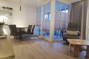 A modern living room with a dining area, large windows, and a view of the outdoors. - in the Atlantik apartment building (Kühlungsborn)