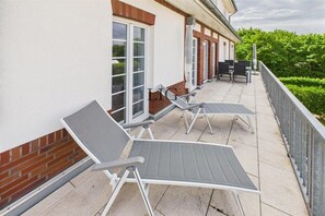 A covered outdoor seating area with metal chairs and tables, adjacent to a building with large windows and a brick facade. - Holiday apartment Küstenglück (Langeoog)