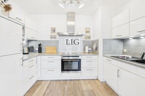 A modern kitchen with white cabinetry, a built-in oven, and a stainless steel range hood. - Holiday apartment Küstenglück (Langeoog)
