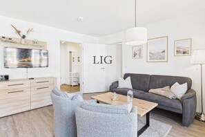 A modern living room with a grey sofa, a wooden coffee table, and a TV on a wooden cabinet. - Holiday apartment Küstenglück (Langeoog)