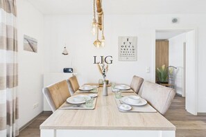 A dining area with a wooden table set for four, surrounded by cushioned chairs. - Holiday apartment Küstenglück (Langeoog)