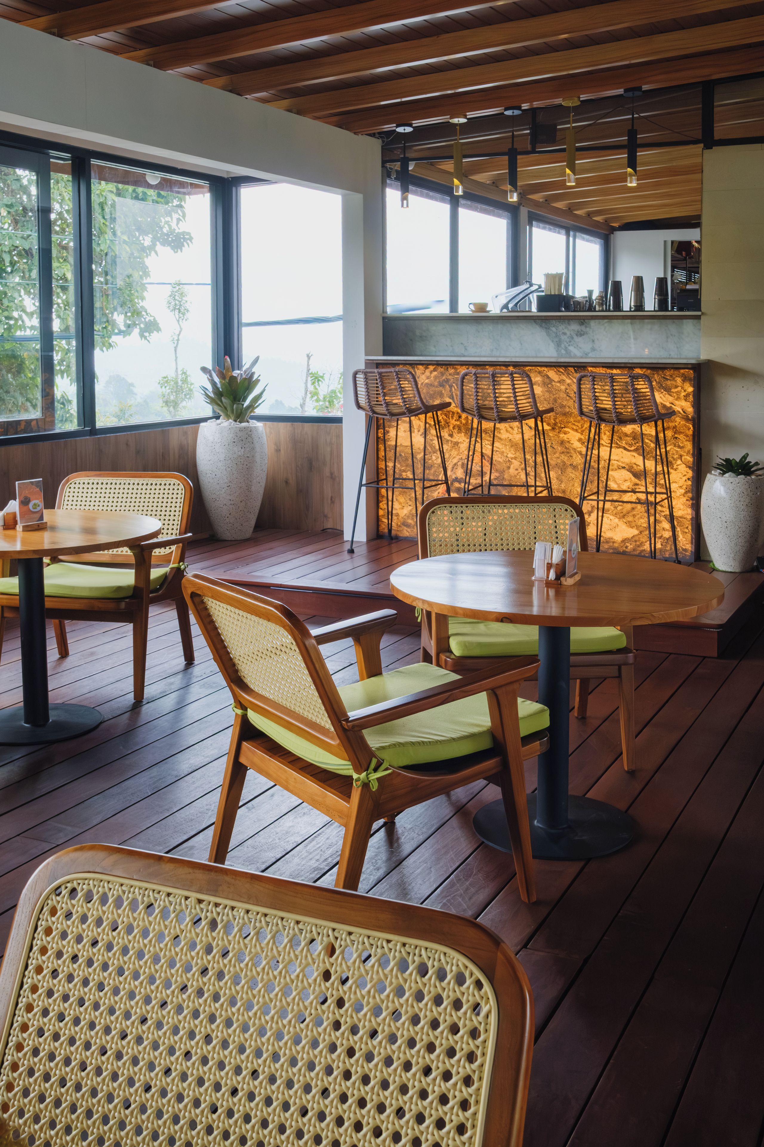 A restaurant interior with wooden flooring, rattan chairs, and a bar area.