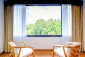Una habitación con dos sillas de madera, un ventanal con cortinas y vistas a un bosque.