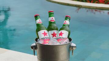 Un balde metálico con tres botellas de cerveza Bintang, colocado al lado de una piscina con vistas despejadas al agua y la vegetación circundante.