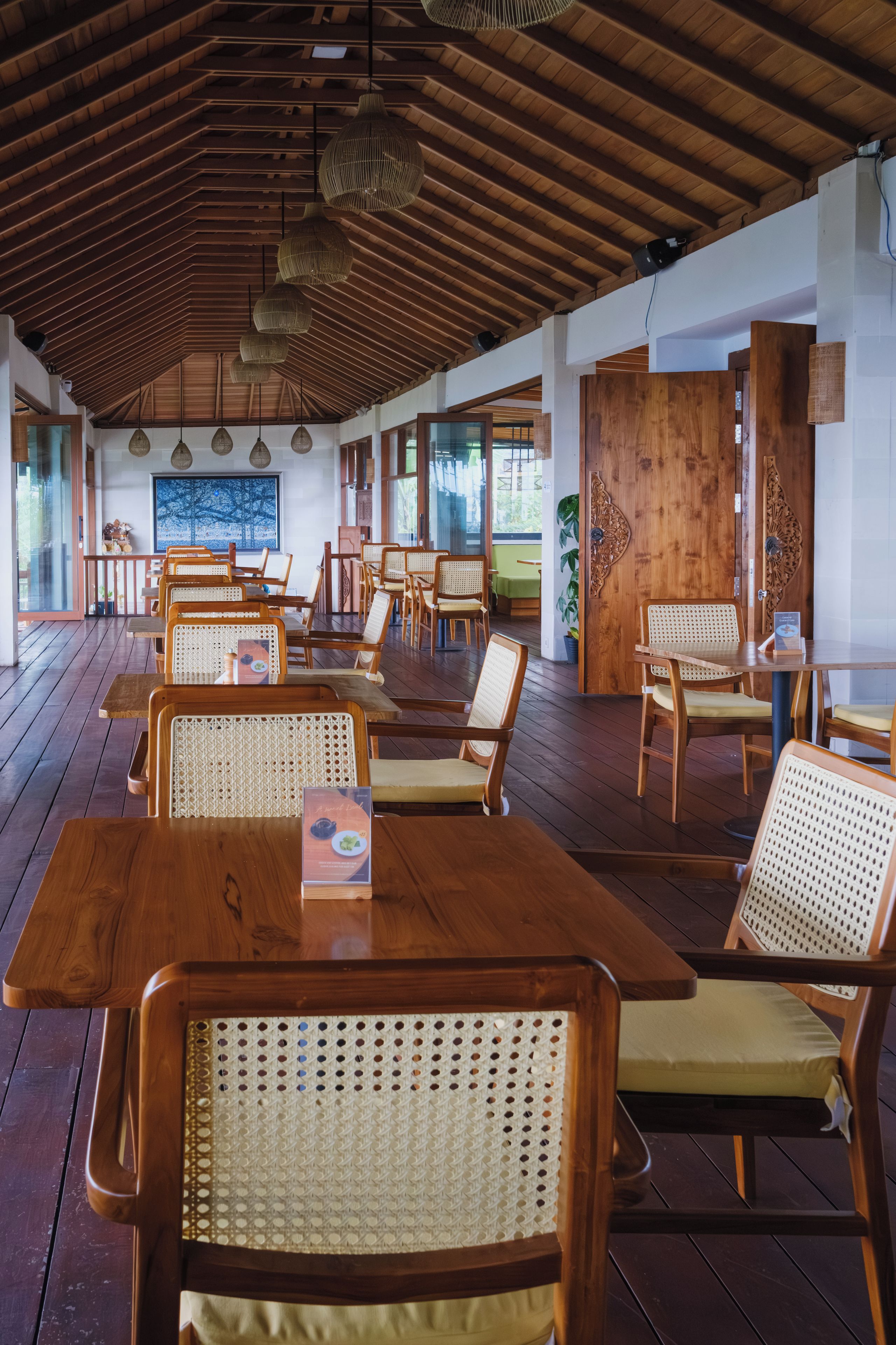 Un restaurante con mesas y sillas de madera, un techo alto con vigas de madera y un gran ventanal con vistas.