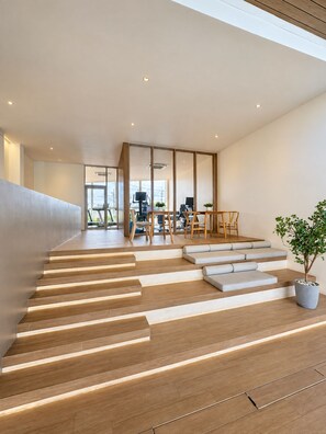 Un interior moderno con una escalera que lleva a una sala de estar, una mesa de comedor con sillas y una planta en maceta.