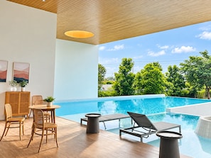 Un área de piscina interior moderna con piso de madera, una mesa de comedor con sillas y sillones de descanso junto a la piscina.