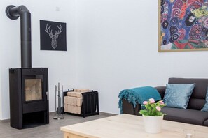 Una sala de estar con un estufa de leña negra, un sofá, una mesa de centro, un cuadro y una chimenea.