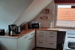 Une petite cuisine équipée d’un four à micro-ondes, d’une machine à café et d’une fenêtre donnant sur un toit recouvert de tuiles.