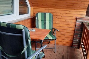 Une terrasse en bois avec une table et deux chaises, une fenêtre et une cheminée en briques.
