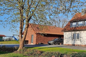 A residential area with a brick house, a car parked in the driveway, and a playground with a slide. - Holiday apartment with 2 bedrooms (Bergen \/ Waldhof)