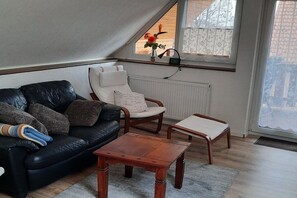 A cozy living room with a black leather sofa, a white armchair, and a wooden coffee table. - Holiday apartment with 2 bedrooms (Bergen \/ Waldhof)