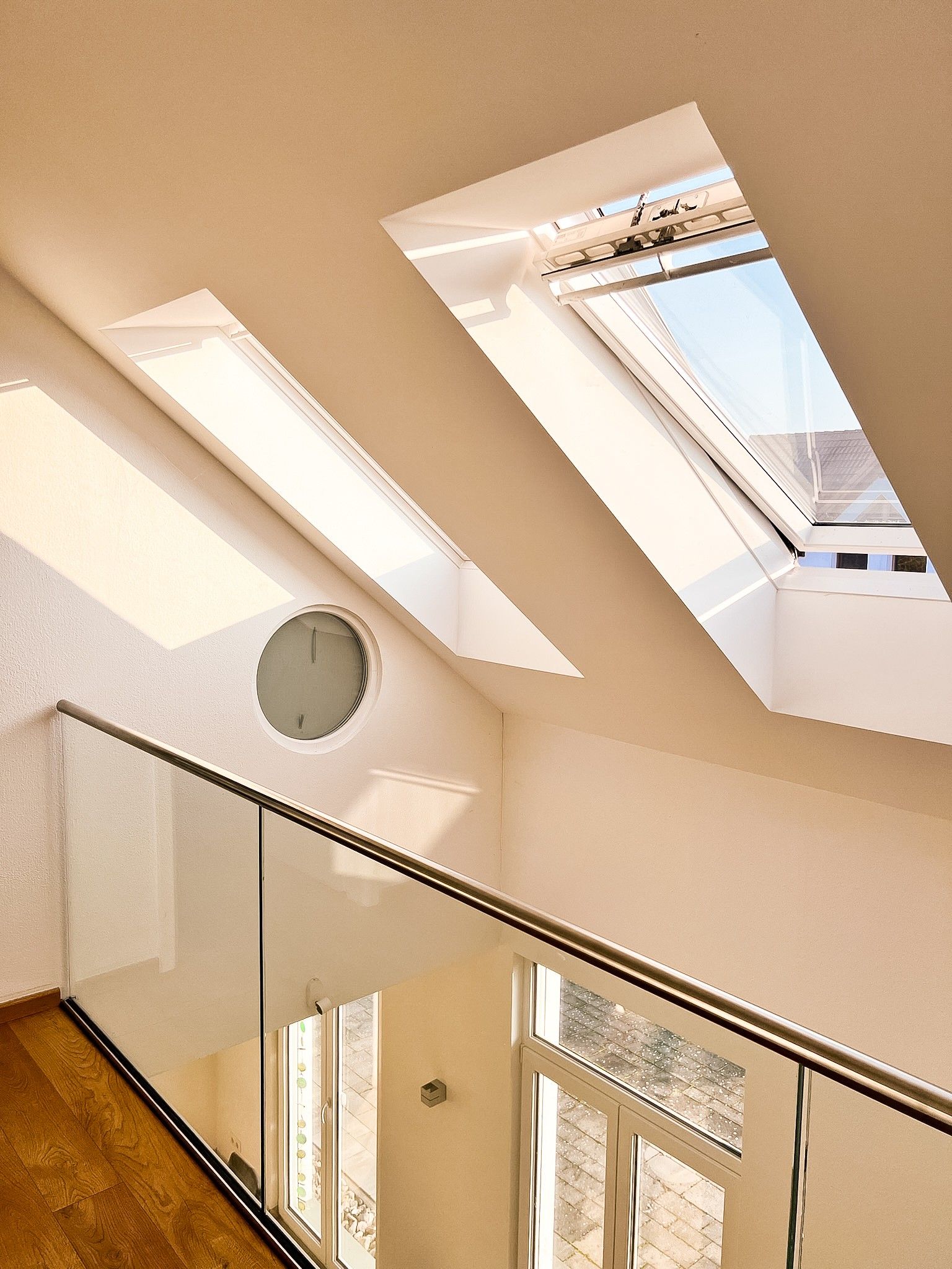 A modern interior with a skylight, a round clock, and a glass staircase.