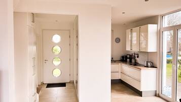 A modern kitchen with a large window, a door with circular windows, and a clock on the wall.