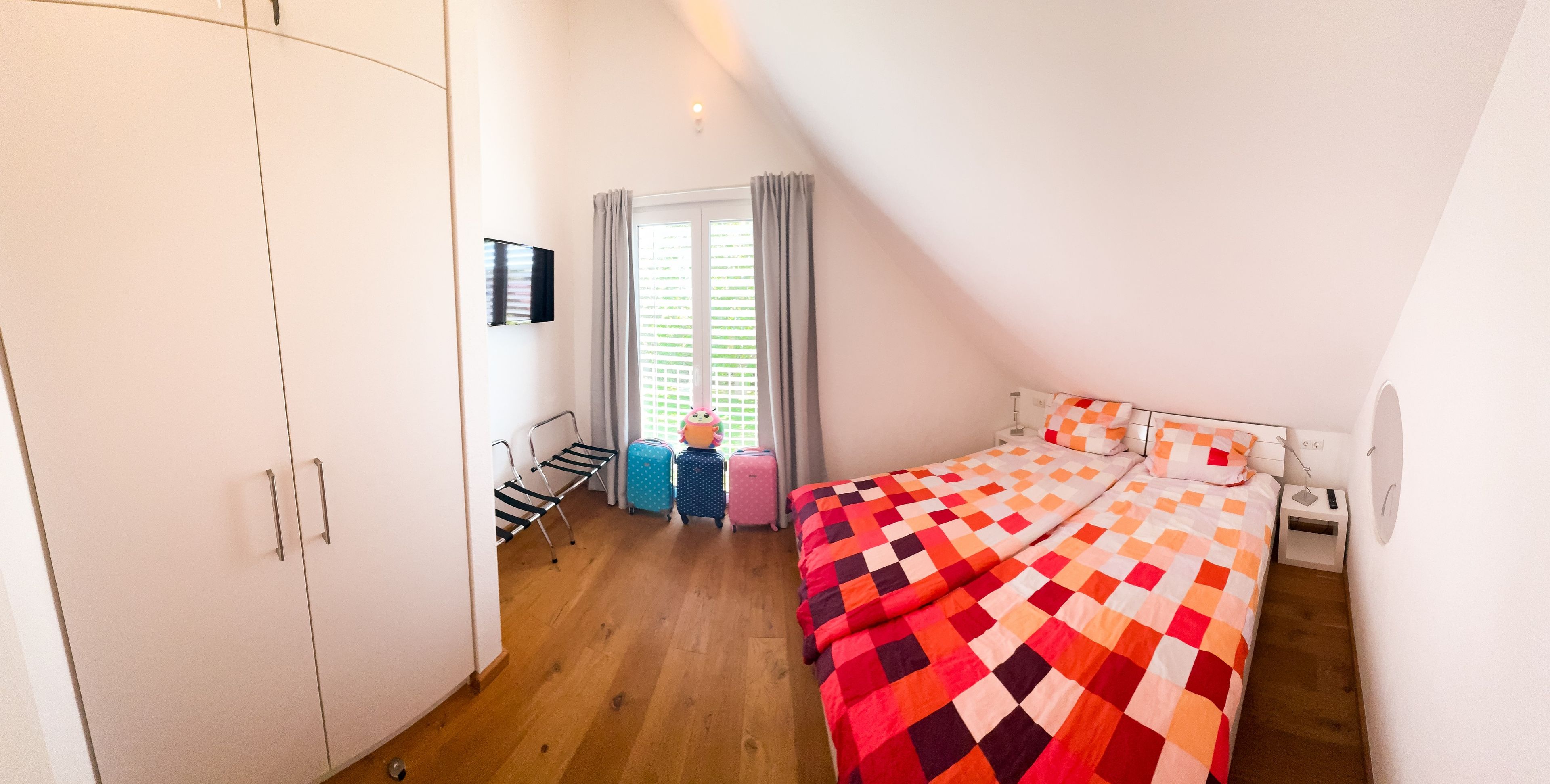 Ein Schlafzimmer mit einem Bett, einem Kleiderschrank, einem Fenster mit Vorhängen und einem Stuhl.