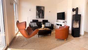 Ein Wohnzimmer mit einer Couch, zwei Sesseln, einem Couchtisch, einem Gemälde, einem Flachbildfernseher und einem Kamin.