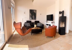 Ein Wohnzimmer mit einer Couch, zwei Sesseln, einem Couchtisch, einem Gemälde, einem Flachbildfernseher und einem Kamin.