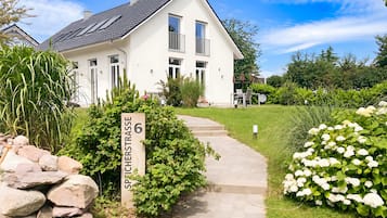 Ein weißes Haus mit einem gepflasterten Weg, der zum Eingang führt, umgeben von Grünflächen und einem Schild mit der Aufschrift 'SPICHESTRASSE 6'.