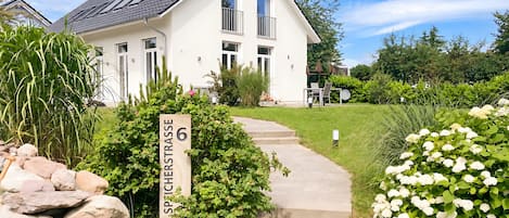 Una casa blanca con un camino pavimentado que conduce a la entrada, rodeada de vegetación y un letrero que dice 'SPICHESTRASSE 6'.