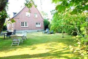 A brick house with a lawn, outdoor seating, and a tree. - Holiday apartment in Wyk with swimming pool (Wyk)