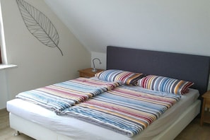 A bed with a striped bedspread and pillows, a bedside table with a lamp, and a wall with a leaf design. - 3 in the periwinkle house (Cuxhaven-Duhnen)