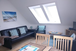 A modern living room with a black leather sofa, a wooden chair, a small round table, and a skylight. - 3 in the periwinkle house (Cuxhaven-Duhnen)