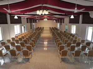A conference room with rows of chairs, ceiling fans, and hanging lights. - Spree One Resort and Convention (Shankhavaram)