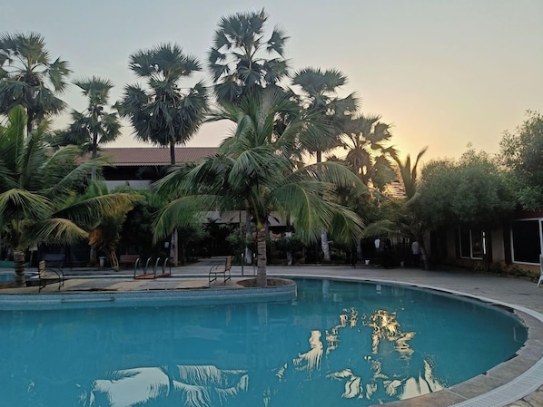 A swimming pool surrounded by palm trees and a building with a red roof. - Spree One Resort and Convention (Shankhavaram)