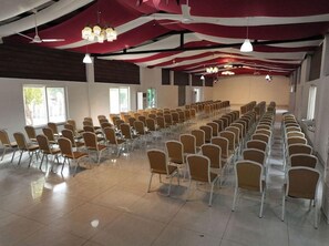 A conference room with rows of chairs, large windows, and a high ceiling with hanging lights. - Spree One Resort and Convention (Shankhavaram)