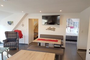 A modern living room with a sofa, a plaid armchair, a wooden coffee table, and a television mounted on the wall. - Holiday apartment with 2 bedrooms (Norden)