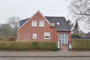 Ein zweistöckiges Backsteinhäuschen mit geneigtem Dach, einer kleinen Veranda und einer sichtbaren Klimaanlage.