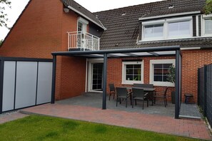 A residential property with a brick exterior, a covered patio area with a table and chairs, and a small garden. - Holiday apartment with 2 bedrooms (Norden)
