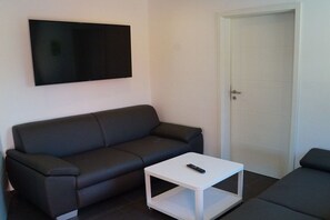 Una sala de estar moderna con un sofá de color oscuro, una mesa de centro blanca y un televisor de pantalla plana montado en la pared.
