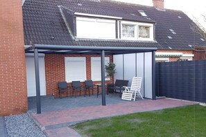 A covered patio area with outdoor seating and a white chair. - Holiday apartment with 2 bedrooms (Norden)
