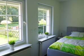 A bedroom with a bed, two windows, a radiator, and a small table. - Holiday apartment with 2 bedrooms (Norden)