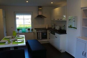 A compact kitchen with white cabinets, a stove, and a window with a view of greenery. - Holiday apartment with 2 bedrooms (Norden)
