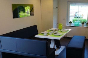 A dining area with a table set for four, a black sofa, and a bench. - Holiday apartment with 2 bedrooms (Norden)