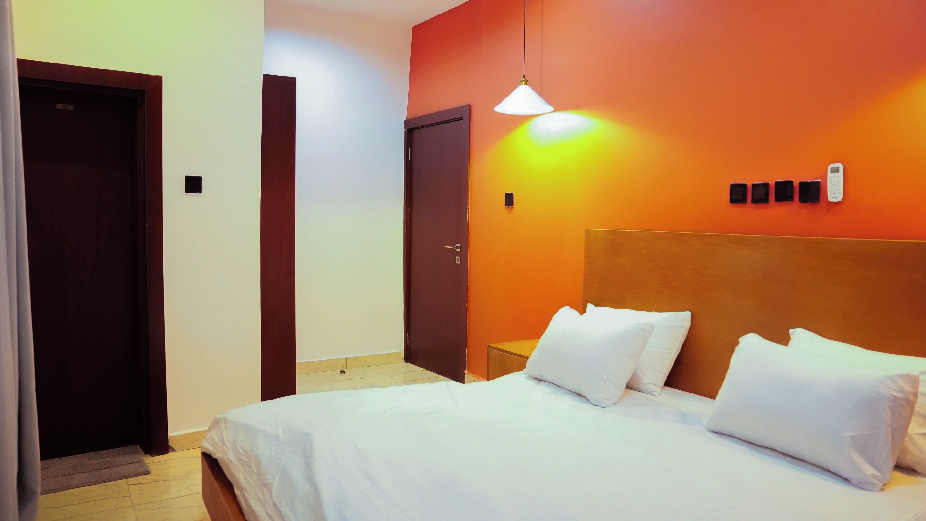 A hotel room with a bed, a door, and a wall-mounted light fixture.